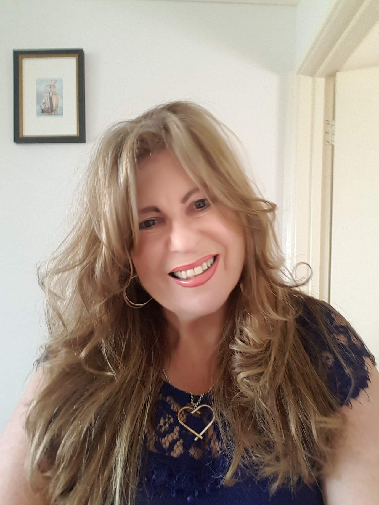 A smiling woman wearing a blue top and heart necklace.