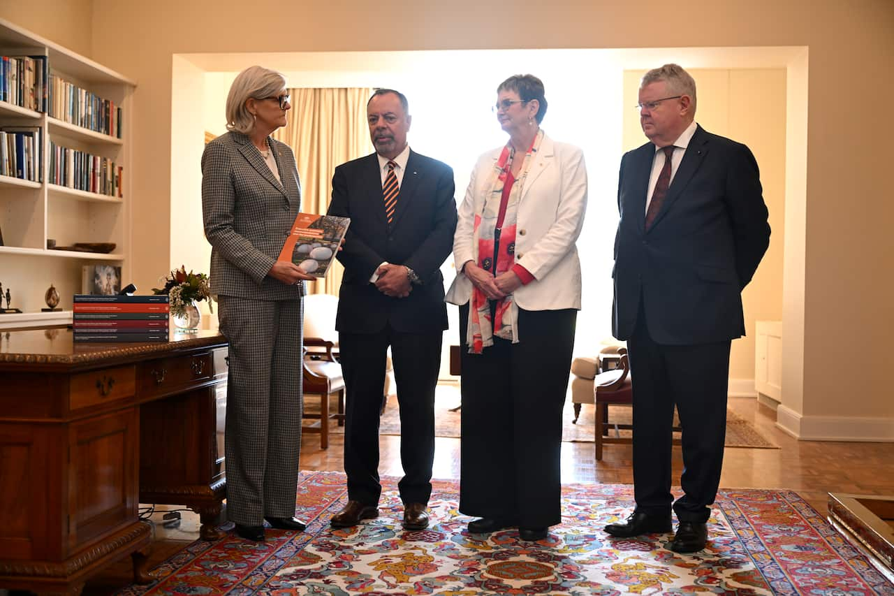 Four people stand in a row, with one holding a report. 