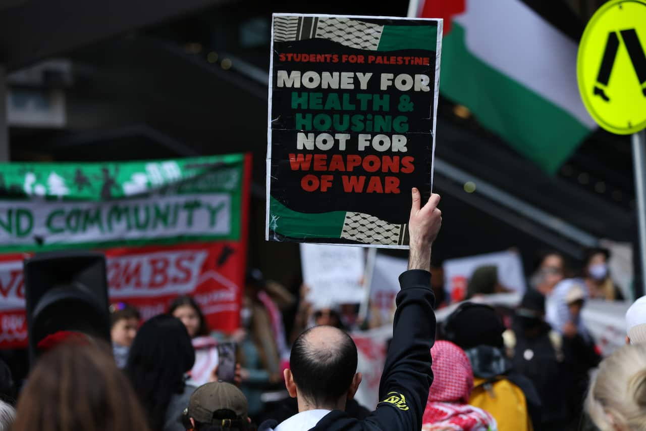 A group of protesters. One person is holding a sign that says "Money for Health and Housing Not for Weapons of War".