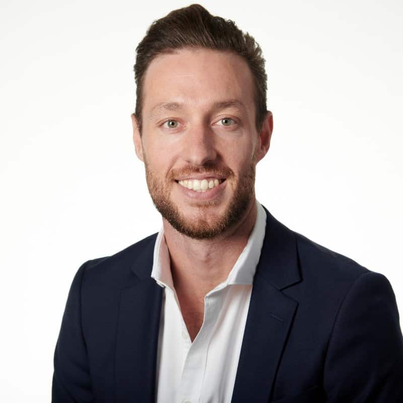 A man in a bue blazer and a white shirt smiles at camera. 