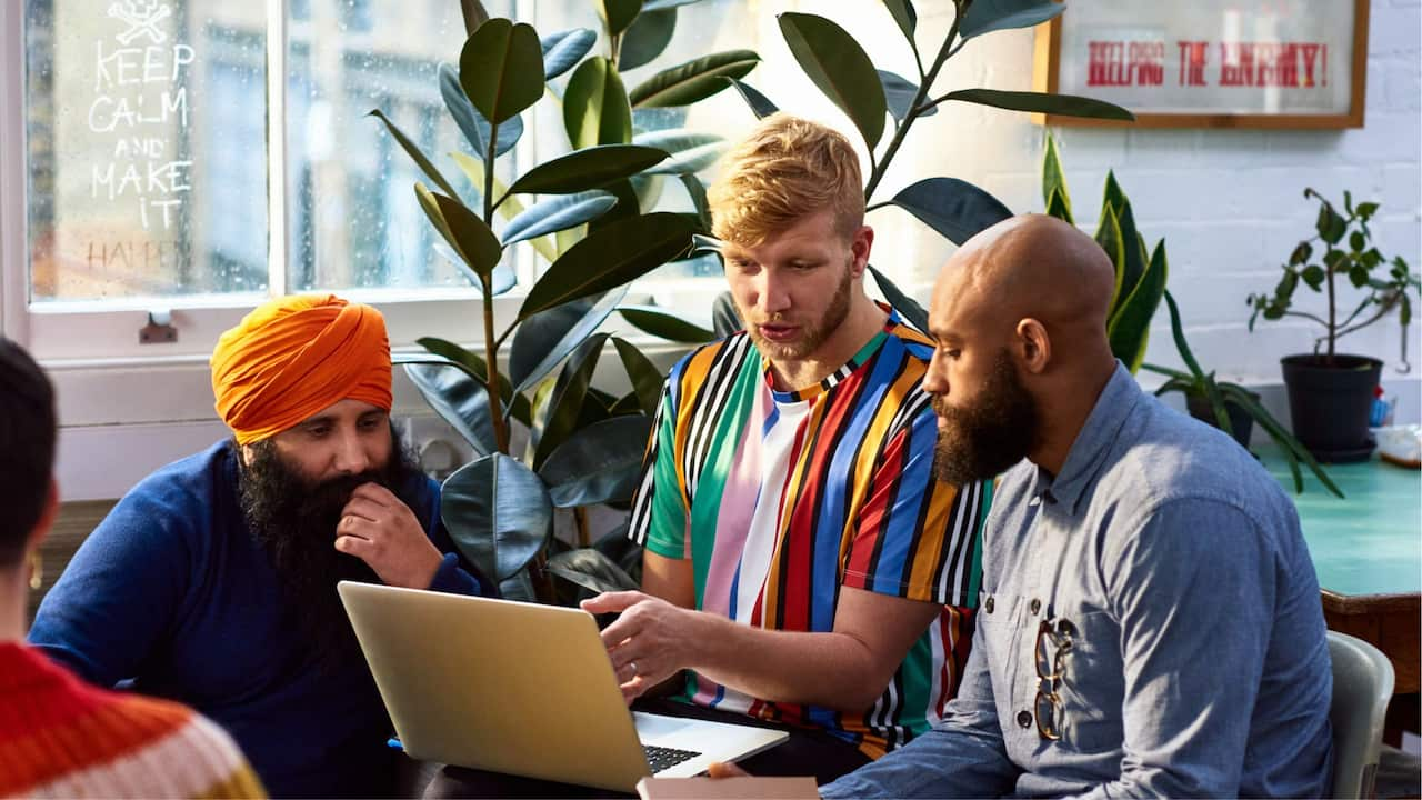 A group of people from multiple ethnicities including a Sikh man, a Caucasian man, and a person of colour working together in a bright office space; indicating social coheasion.