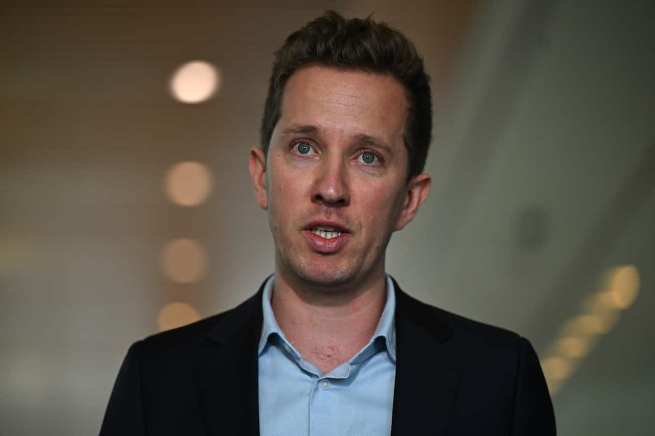 A man wearing a blue shirt and black blazer is speaking.