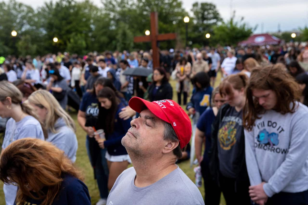 Mourners pray at a vigil in a park.