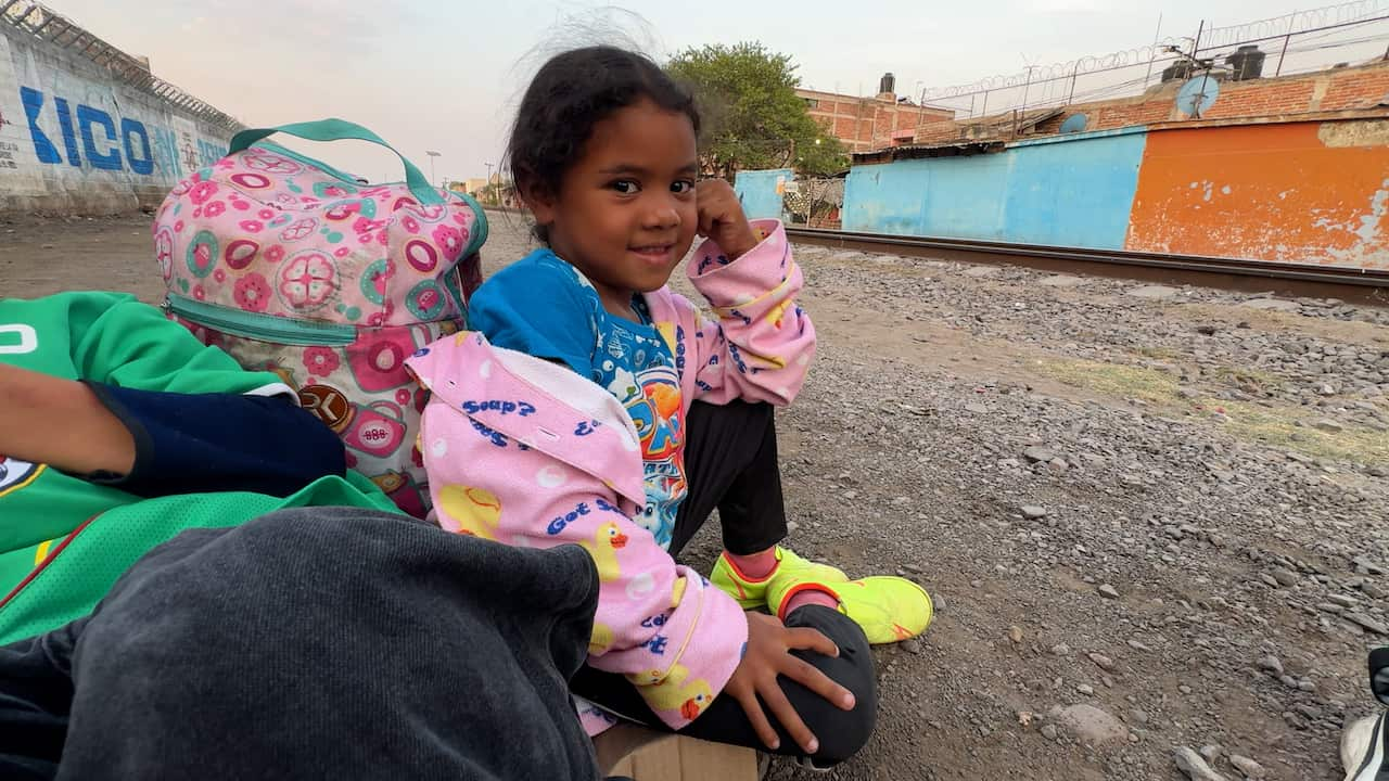 A small girls sits with luggage on the ground and smiles at the camera