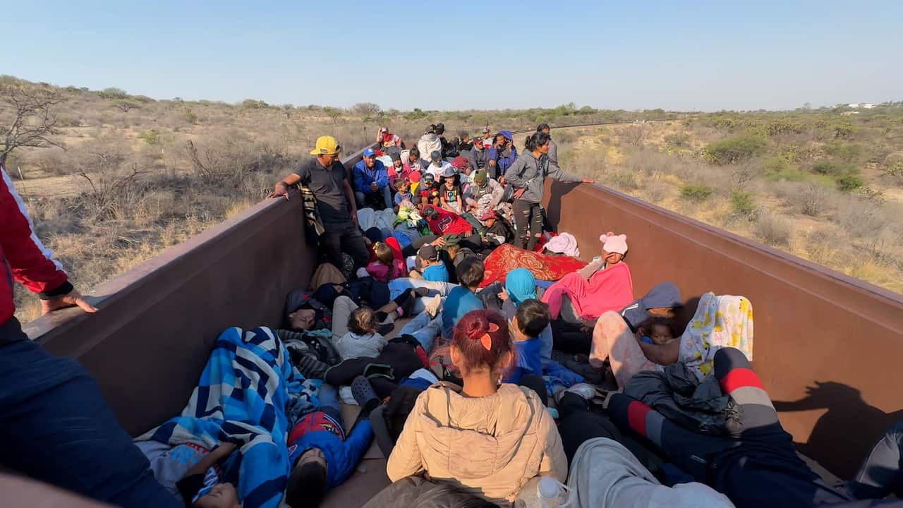 Migrants sleep in a large red wagon under blankets sheltering from the sun 