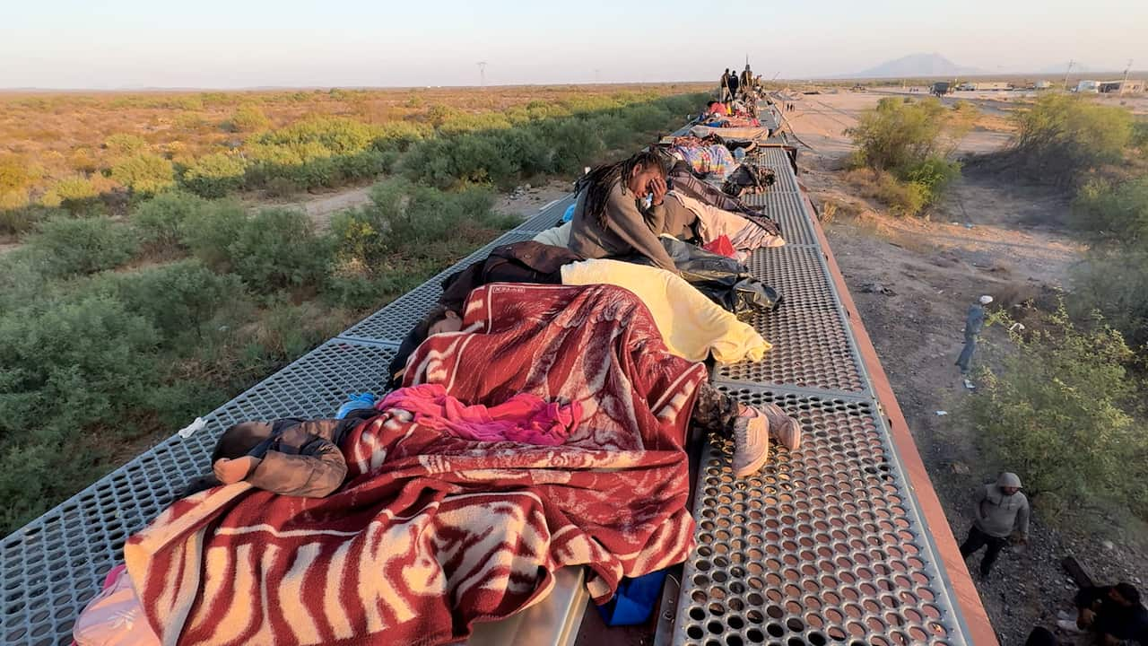 Migrants sleep under red and yellow blakets atop the train 