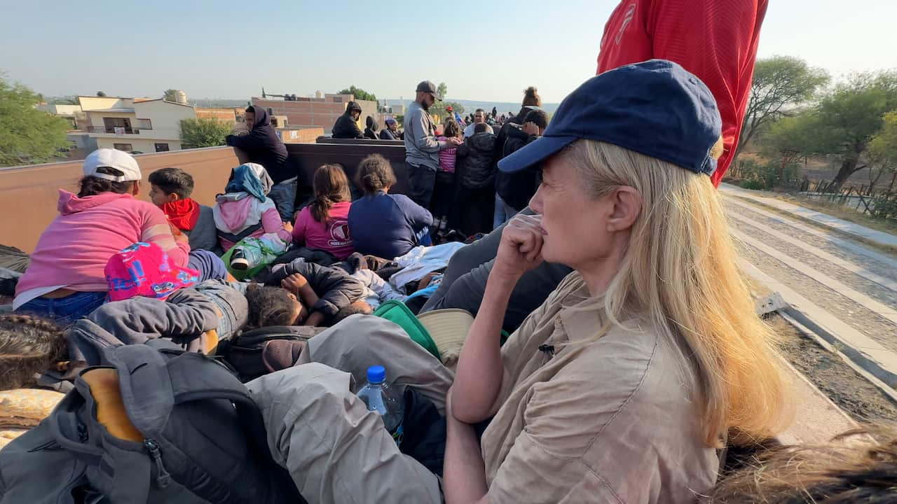 A woman wearing a blue cap sits on the train among people. 