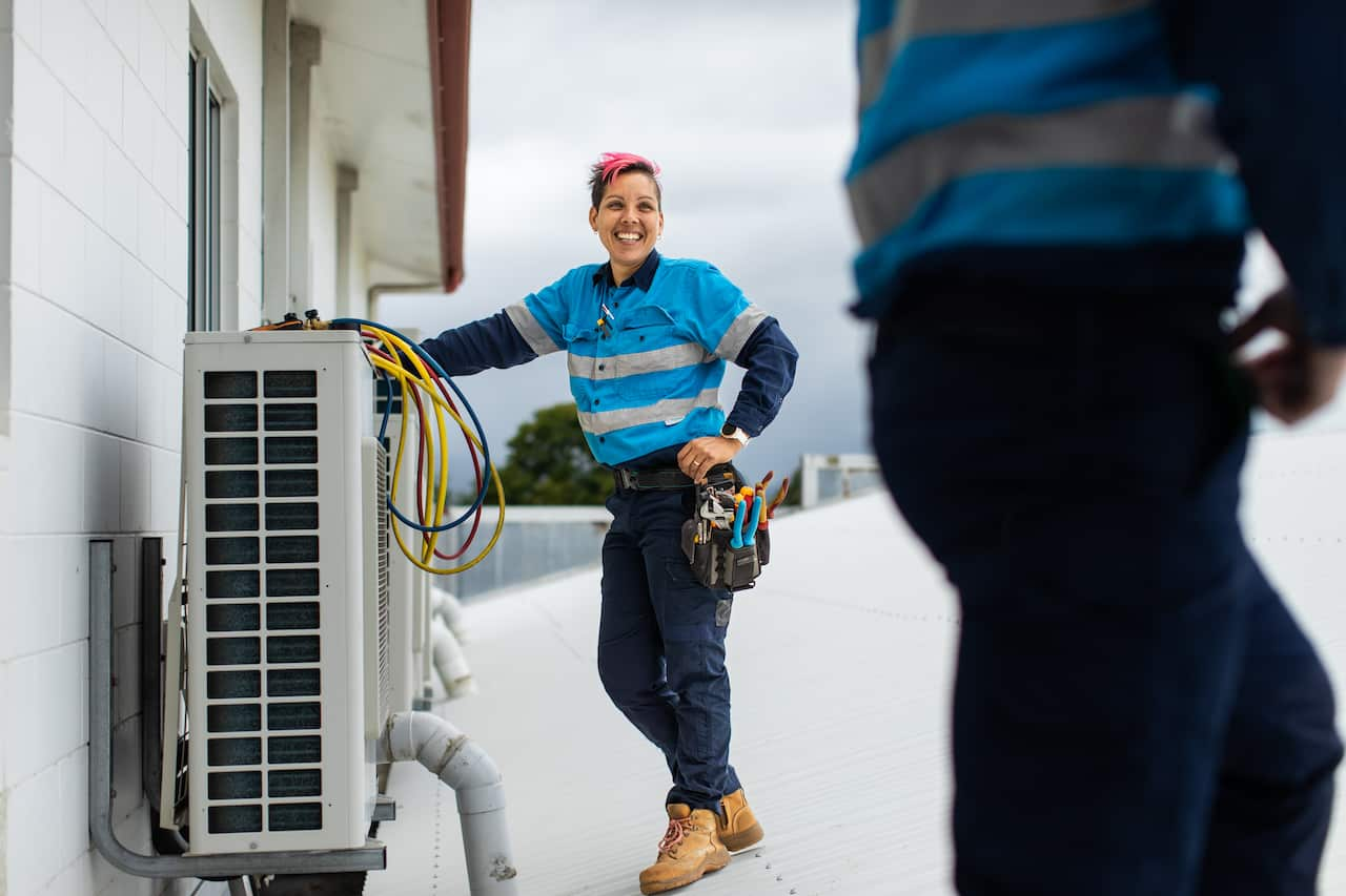 Female tradesperson on a roof working on an air-conditioning unit.