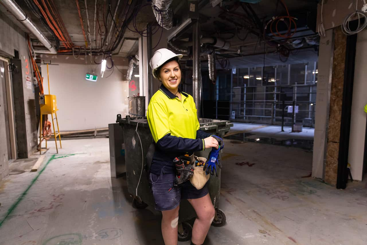 A woman wearing a high vis shirt and a hard hat at a construction site.