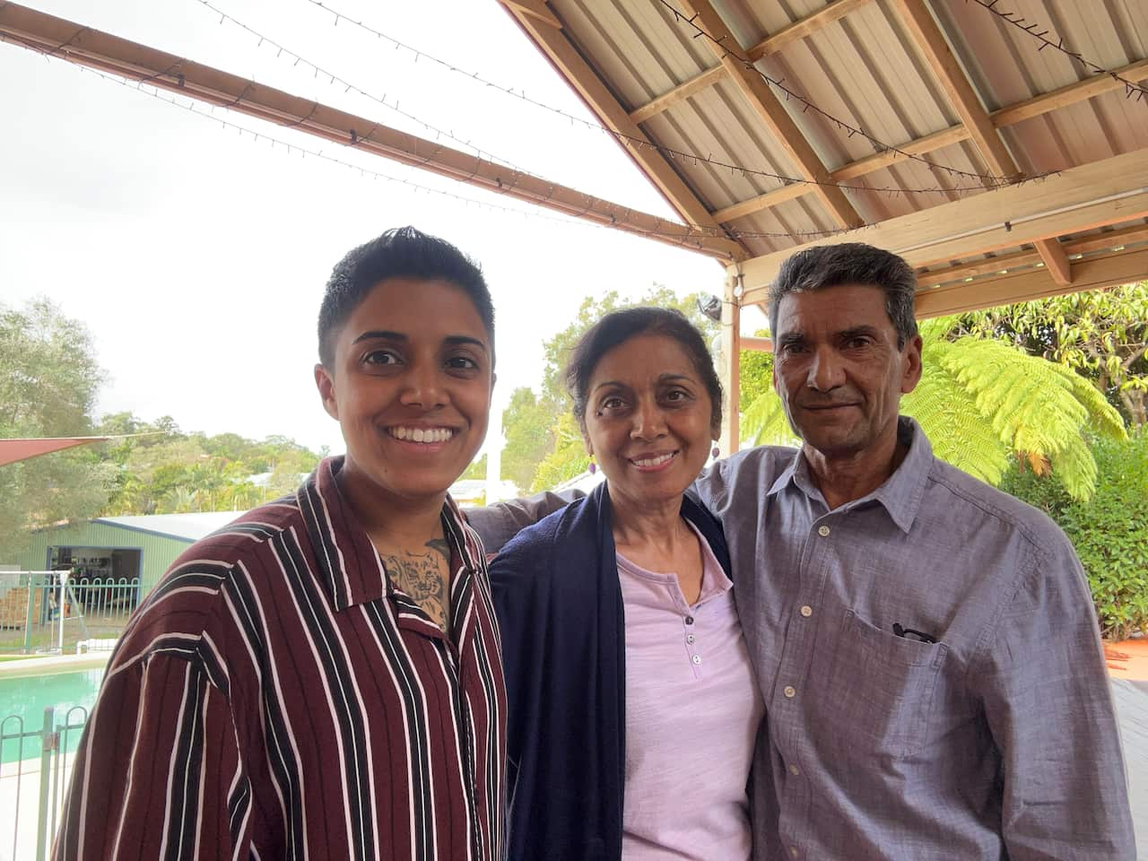 A woman wearing a stripey shirt poses with her parents.