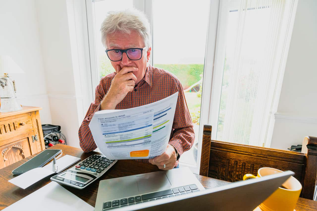 A senior man checks his bills while sitting at a table.