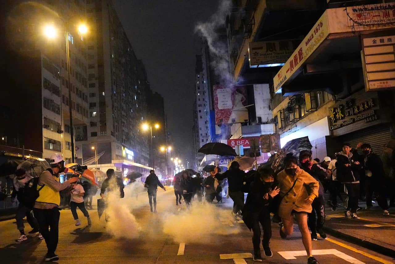 A group of protesters running through the streets amid tear gas.