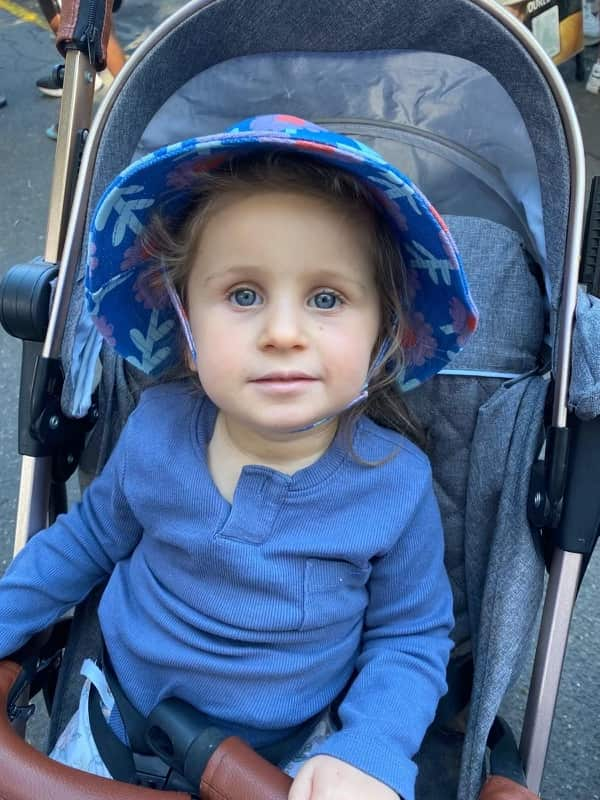 A three-year-old girl in a blue shirt sits in a pram.