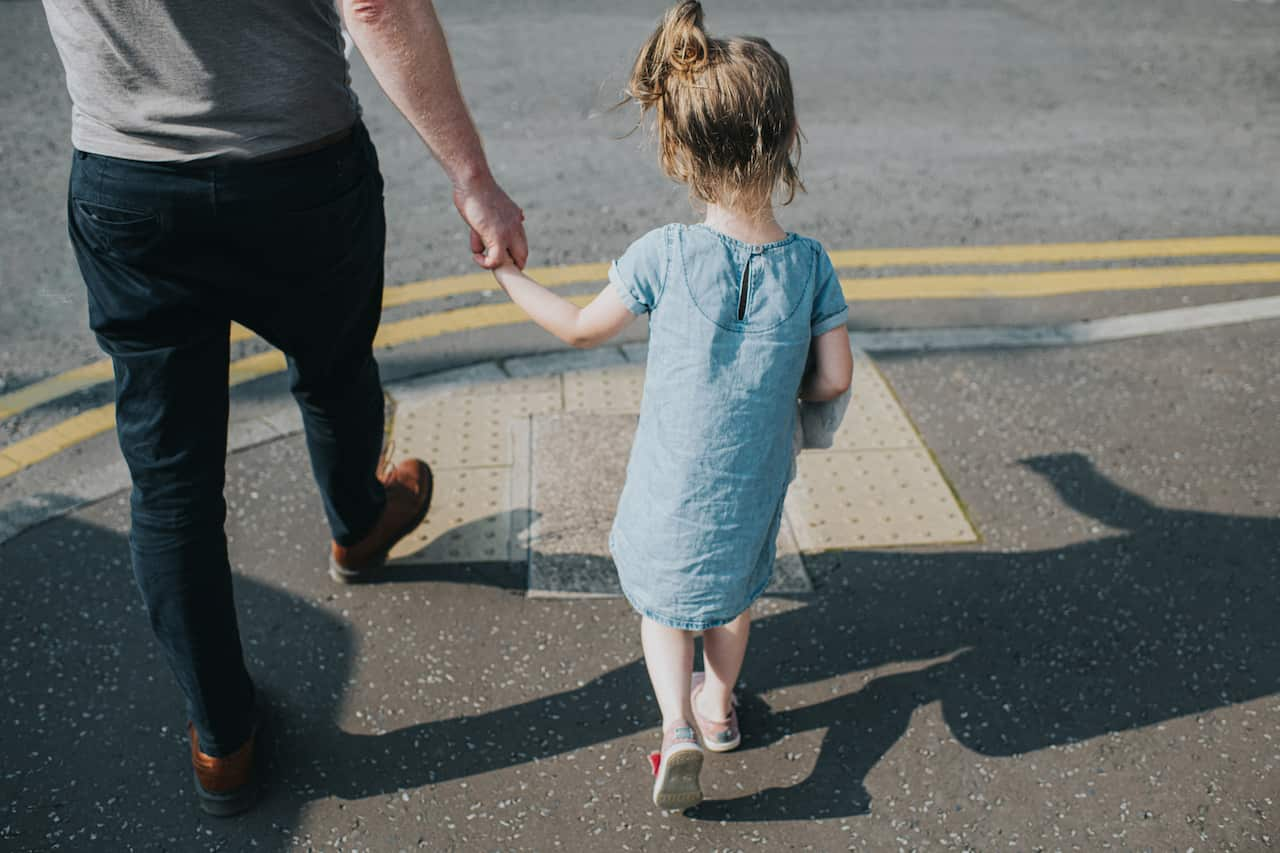 A little girl holding her father's hand, about to cross a road.