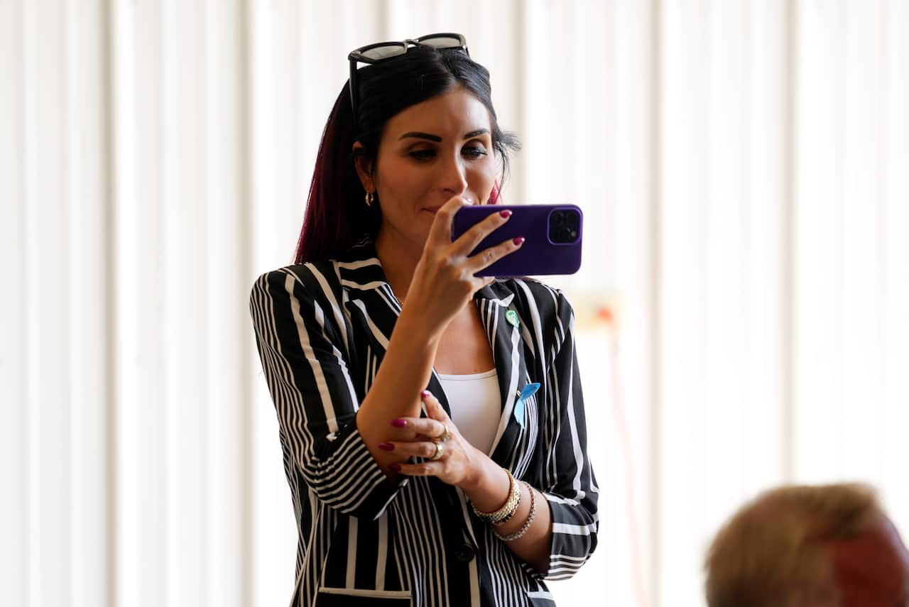 A woman wearing a stripy blazer holding her phone horizontally in her hand.