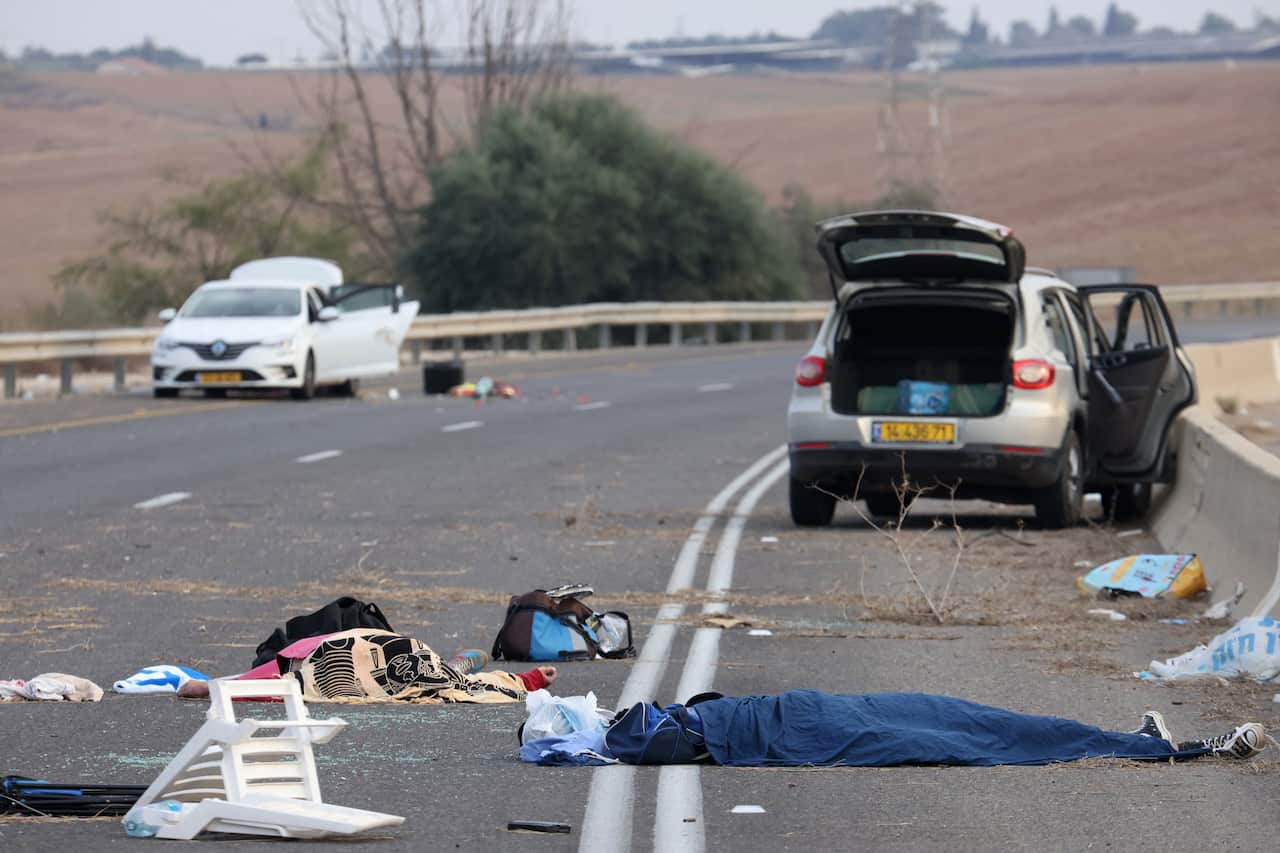 Two cars are stopped on the road with their doors open, in the foreground, what appears to be bodies can be seen.