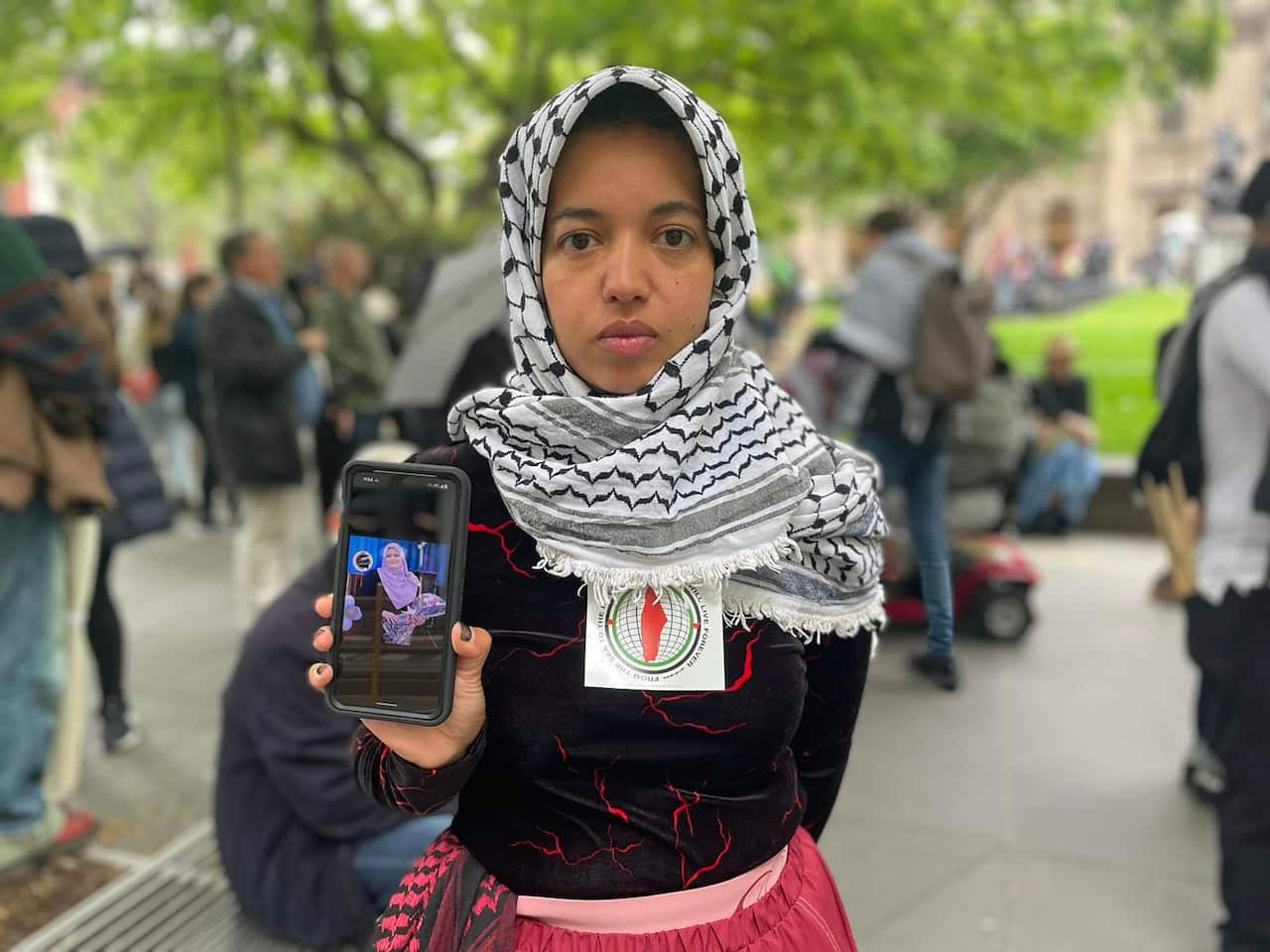 A woman wearing a keffiyeh and holding up her phone