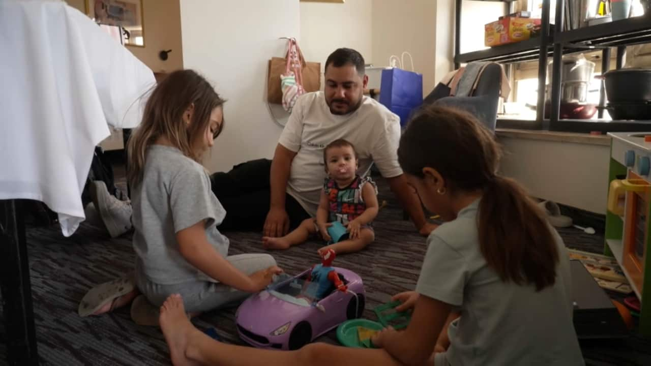 Two young girls, a baby and a man sit on the floor of a hotel room playing with toys.