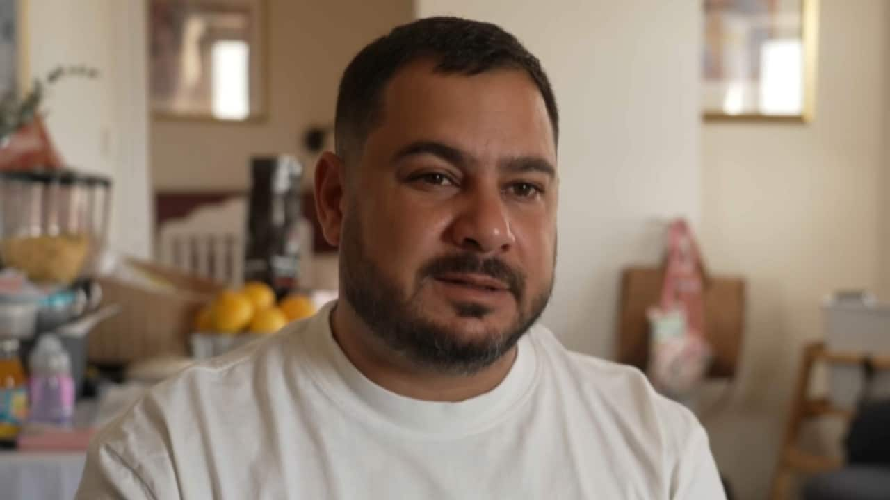 A man with facial hair wearing a white t-shirt.