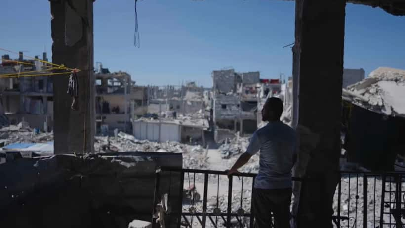 A man standing in the ruins of a building in Gaza looking out at destroyed buildings