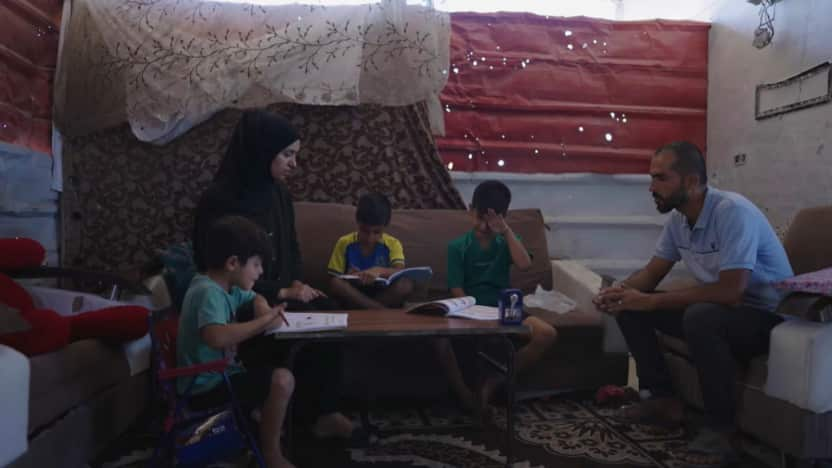 A three children woman in a black hair covering, and a man sit around a coffee table in a loungeroom