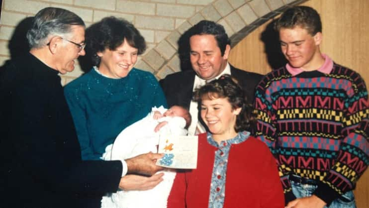 A family with a teenage son, younger daughter and baby in a church standing next to a priest.