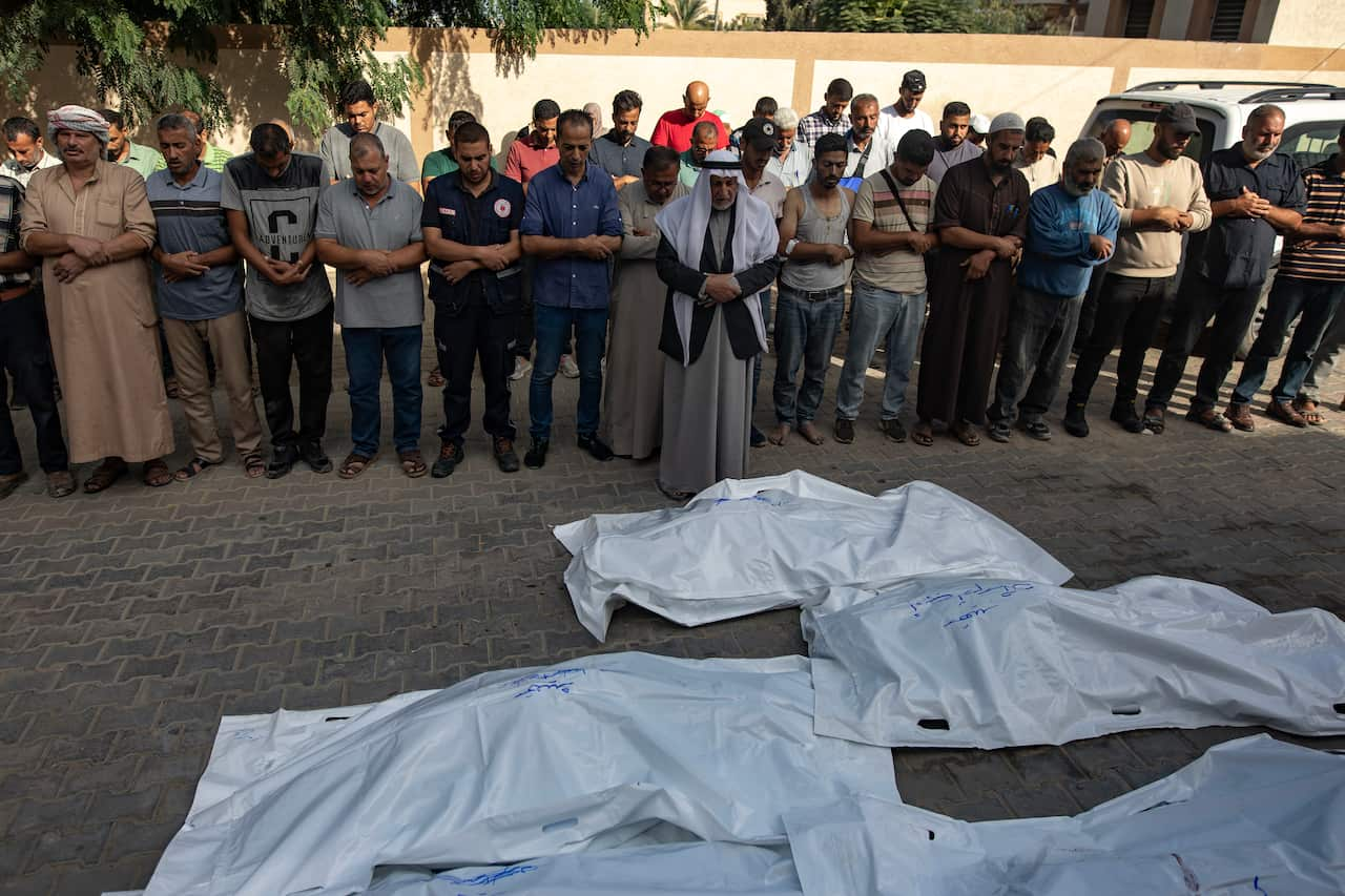 A group of men standing over large, white bags laying on the ground.