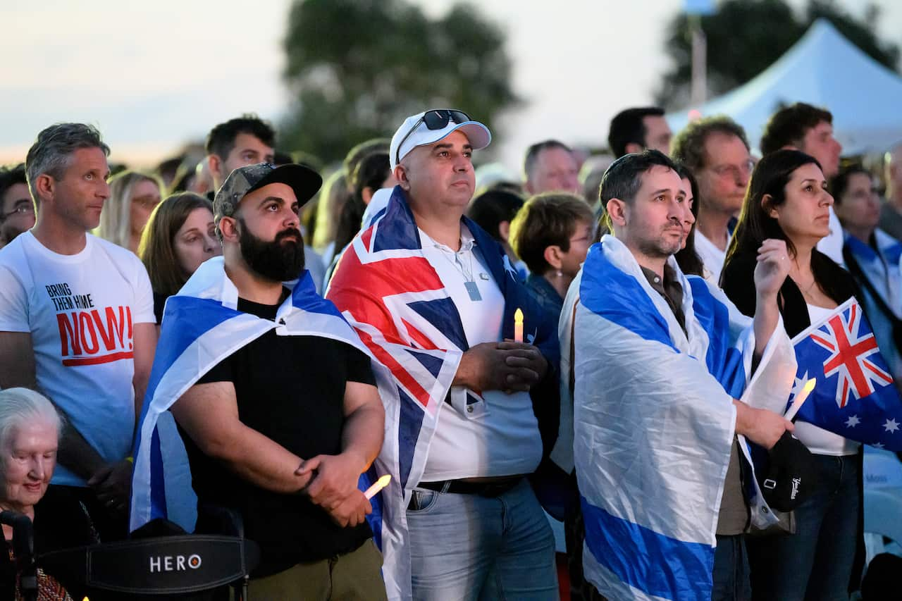 A group of people with Israeli and Australian flags visible draped over some people's shoulders