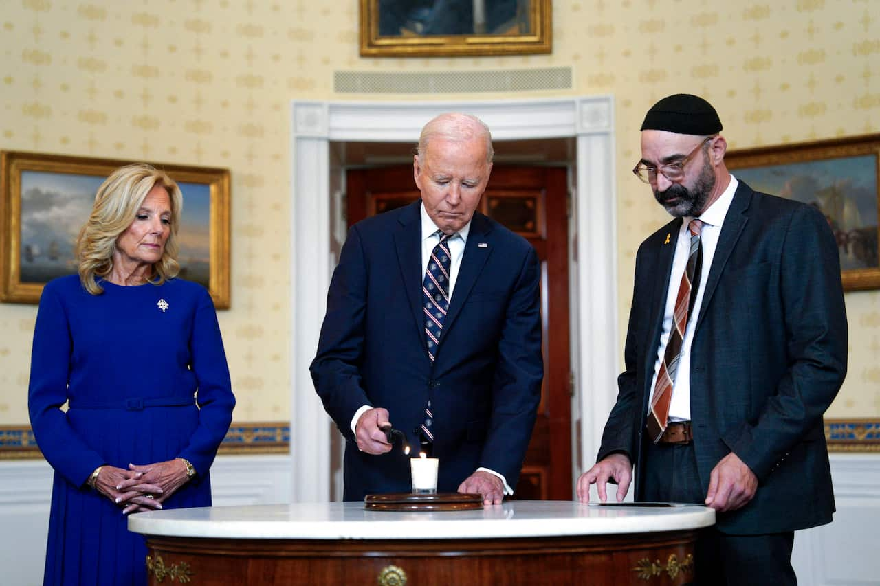 A man in a suit lights a candle with a woman to his left and another man to his right 