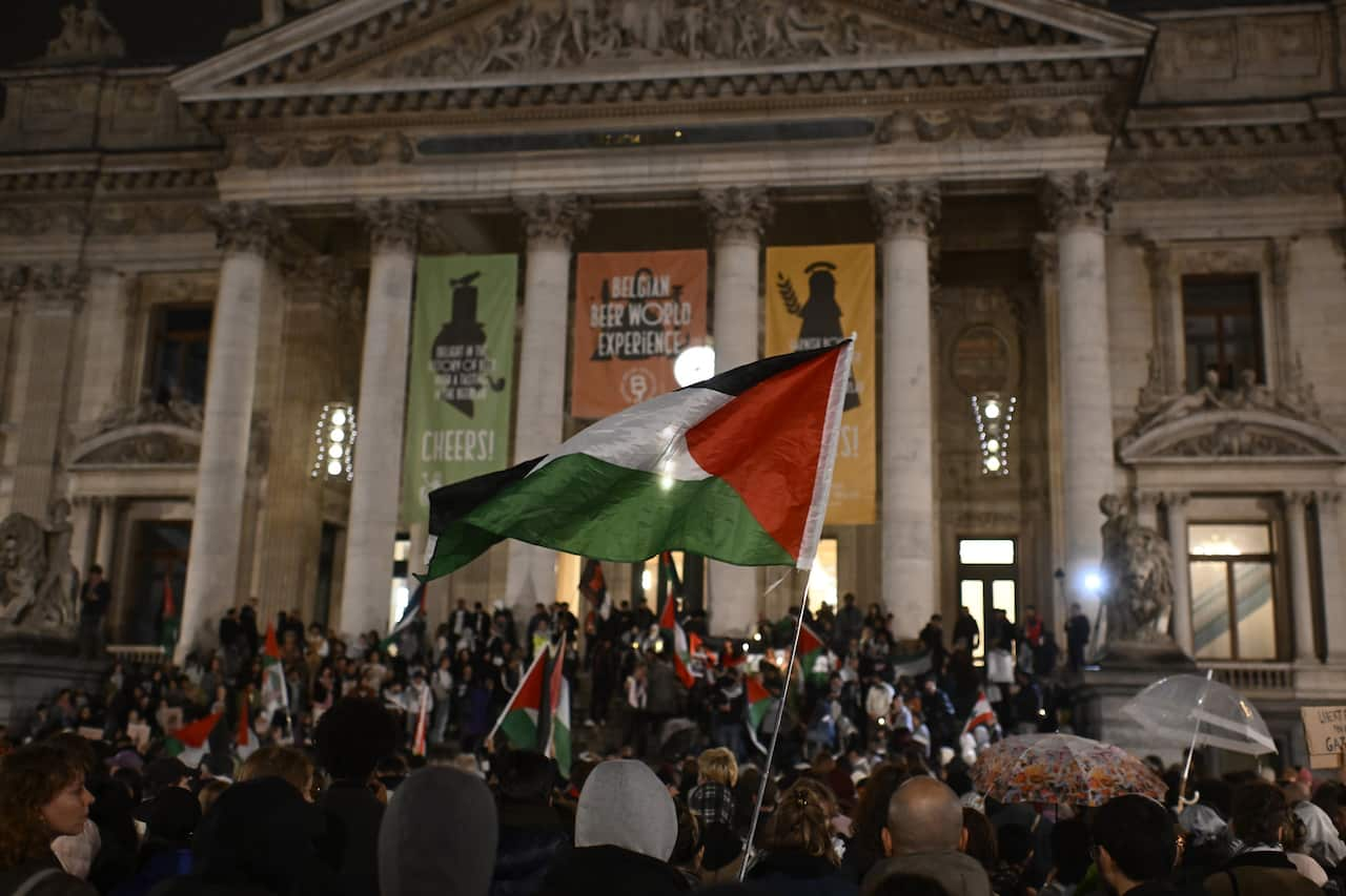 A crowd of people at night with Palestinian flags visible 